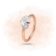 Rose gold ring with pear-shaped diamonds on a soft pink background